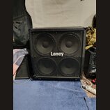 Černý basový reproduktor s kovovou mřížkou, za kterou jsou vidět čtyři velké membrány. Uprostřed mřížky je bílý nápis Laney. Povrch je v dobrém stavu…