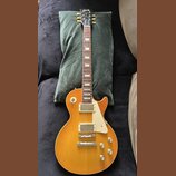 Elektrická kytara s žlutým gradientním lakem a bílým plechtrzem. Na hlavě hředu je viditelné logo Gibson. Nástroj má dva humbuckery, čtyři ovládací k…