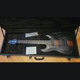 Černá elektrická kytara v otevřeném černém kufru. Na hlavě je logo CHAPMAN GUITARS a na hrazence symbol nekonečna. Tělo kytary je matně černé s vidit…