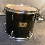 Černý buben s chromovaným kováním a bílým blánou. Na korpusu je zlatý štítek s nápisy Pearl, Masters Studio a pod nimi menší text MADE IN TAIWAN. Pov…