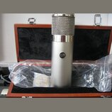 Stříbrný kondenzátorový mikrofon s kovovou síťkou v horní části. Na těle mikrofonu je umístěno kulaté logo s nápisem UA. Mikrofon je umístěn v otevře…