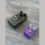Na fotografii jsou dva efektové pedály na dřevěné podlaze. Větší pedál je olivově zelený s nápisy BIG MUFF π, electro-harmonix a ОВЕРДРАЙВ. Menší ped…