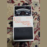 Bílý kytarový ladič značky BOSS, model Chromatic Tuner TU-3. Na horní straně je analogový displej s nápisy CHECK, PITCH a označením tónů. V horní čás…