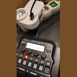 Černý kytarový procesor s nápisy ZOOM G1X FOUR a Multi-Effects Processor. Na displeji je zobrazen text 24 RocknRoll. Zařízení je připojeno k bílému n…