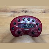 Červený kytarový procesor značky LINE 6. Na horní části jsou ovládací knoflíky s popisky DRIVE, BASS, CHANNEL a REVERB, uprostřed je nápis POD. Spodn…