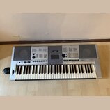 Stříbrošedý digitální klavír s bílými a černými klávesami. Na horním panelu je uprostřed logo YAMAHA a vpravo nápis PSR-E403. Nástroj obsahuje disple…