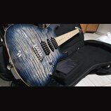 Elektrická kytara s modrým plamenovitým povrchem těla a světlým hnedým hmatníkem. Nástroj má tři humbuckery, chromovaný most a dva ovládací knoflíky.…