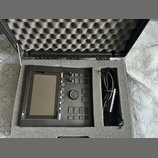 Černý elektronický kontrolér s displejem, umístěný v polstrovaném transportním kufru. Na levé straně je svisle napsaný bílý nápis DIVO. Zařízení obsa…