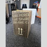 Dřevěný cajón s tmavým povrchem a světlými hranami. Na přední straně je bílý nápis „271-CAJO / HERK PERCU / 2,60' SNAR / 2IN-ONE CA“ a pod ním symbol…
