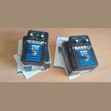 Dvě černé efektové pedály s modrými pruhy, umístěné na svých krabicích. Levý pedál nese nápisy MULTICOMP, True Dual Band Compressor a logo EBS. Pravý…