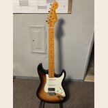Elektrická kytara s trupem v barevnosti sunburst a bílým pickguardem. Na hlavě hmatníku je viditelné logo Squier. Krk a hmatník jsou vyrobeny ze svět…
