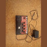 Kytarový efekt pedál s černým povrchem a červenými ovládacími knoflíky. Na zařízení jsou viditelné nápisy RADIAL, HOT BRITISH DISTORTION a LINE 6. V…