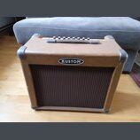 Kytarový kombo zesilovač v hnědém vinylovém potahu s kovovými rohy. Na přední straně je umístěno oválné logo s nápisem KUSTOM a pod ním hnědý textiln…