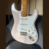 Elektrická kytara s bílým tělem a hnědým dřevěným hmatníkem. Nástroj má bílý pickguard, tři snímače a tři ovládací knoflíky s nápisy VOLUME, TONE a T…