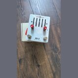 Bílý kytarový efekt s nápisy HW-2 a ONEDER EFFECTS. Zařízení má čtyři posuvníky s popisky GAIN, BASS, MID a TREBLE, dva červené otočné knoflíky s pop…