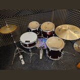 Sada červených bubnů s kovovým hardwarem a mosaznými činely. Na blbáku je vidět logo Sabian, na ostatních bubnech jsou nečitelné loga. Soubor obsahuj…