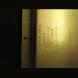 Detail zlatavého kovového povrchu s vyrytými nápisy. Je zde uveden text „scoutronics“, „CARY, IL“, „PAT 2,982,819“, „3,106,610“ a „MADE IN U.S.A.“. V…