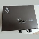Černý kovový box s nápisem Power ATTENUATOR a grafickým symbolem zvukové vlny. V levém horním rohu je bílé logo znázornující stylizované písmeno H s…