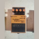 Oranžový efekt pedál s černým ovládacím panelem a černým spodním spínačem. Na zařízení jsou nápisy TURBO Distortion DS-2 a logo BOSS. Horní panel obs…