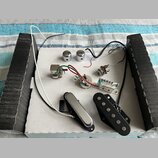 Sada elektroniky pro elektrickou kytaru rozmístěná na bílém podkladu. Soubor obsahuje dva chromované knofíky, jeden přepínač, potenciometr, vstupní j…