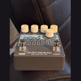 Šedý kytarový efekt s bílými oválnými knoflíky. Na horní straně je nápis bass MONO SYNTH a v dolní části značka electro-harmonix NEW YORK CITY, USA.…