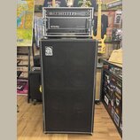 Sada basového zesilovače a reproduktorové skříně v černé barvě. Horní část obsahuje rack s nápisy SVPCL a ampeg SVT-300. Spodní reproduktorová skříně…