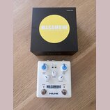 Bílý kytarový efekt s modrými knoflíky a nápisem MASAMUNE —booster & kompressor— a logem NUX. Na pedálu jsou ovládací prvky BOOST LEVEL, BLEND, KOMP…