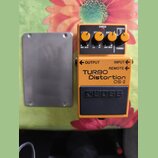 Kytarový efekt pedál oranžové barvy s černým spínacím tlačítkem. Na přední straně je nápis TURBO Distortion DS-2 a logo BOSS. V horní části jsou čtyř…