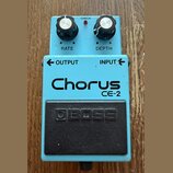 Modrý efekt pedál s nápisy Chorus a CE-2. Na horní části jsou dva černé ovratovky s popisky RATE a DEPTH, červená kontrolka CHECK a vstupy OUTPUT a I…