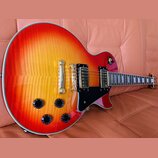 Elektrická kytara s trupem ve tvaru Les Paul v červeno-žlutém sunburst provedení s viditnou strukturou dřeva. Nástroj má dva humbuckery, čtyři černé…