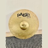 Kruhové mosazný činel s viditelným povrchovým opotřebením a skvrnami. Na povrchu je černý nápis pAiste, pod ním text 16" CRASH a vedle loga označení…