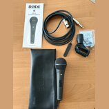 Na fotografii je černý dynamický mikrofon s kovovou síťkou, černý kožený obal s vyraženým nápisem RODE a černý kabel s konektory XLR a 6,35mm jack. S…