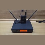 Černý bezdrátový přijímač s dvěma anténami a nápisem LD SYSTEMS WS1000/QR. Na přední straně je oranžový displej s hodnotou 826.300 MHz a řada kontrol…