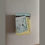 Fotografie znázorňuje papírovou krabici s produktem. Na krabici je zobrazen přístroj v béžové barvě s ovládacími knoflíky a přepínači, doprovázený ná…