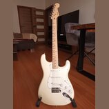 Bílá elektrická kytara typu Stratocaster s bílým pickguardem a javorovým hnedým hmatníkem. Na hlavě nástroje je viditelné logo Squier. Kytara má tři…
