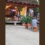 Fotografie zachicuje muzikanta na dřevěném pódiu, který hraje na akustickou kytaru světlé barvy. Vedle něj je umístěn mikrofon na stativu a černý rep…