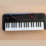 Černý přenosný digitální klavír s bílými a černými klávesami. Na levé straně je bílý nápis YAMAHA a model PSS-A50. Přístroj má ovládací panel s různý…