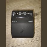 Černý kytarový efekt s nápisy OPUS a AMP SIM DynIR ENGINE. Zařízení má dva ovládací knoflíky a tlačítka s popisky PERFOR., PRESET, VOLUME, MENU, PARA…