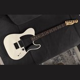 Bílá elektrická kytara s černým pickguardem a hnědým hmatníkem. Na hlavě je vidět nápis Squier by Fender a TELECASTER. Kytara má jeden snímač u kobyl…
