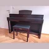 Tmavně hnědé piano s doprovodnou stoličkou v odpovídající barvě. Na horní části piana i na přední straně stoličky je zlatým písmem nápis YAMAHA. Nást…