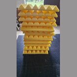 Stoh žlutých akustických absorbů z pěny s pyramidovým povrchem. Panely jsou naskládány na sebe na tmavém podkladu. Na fotografiích nejsou viditelné ž…
