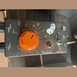 Černý efekt pedál s oranžovými grafickými prvky a velkým oranžovým otočným ovladačem. Na povrchu jsou bílé nápisy record, reset, output phones a on/o…