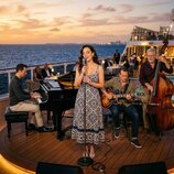 Fotografie zachicuje hudební kapelu na palubě lodi. Je zde vidět černý křídlový klavír s nápisem STEINWAY & SONS, akustická kytara v hnědém provedení…