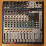 Míčovací pult značky Soundcraft, model Signature 12. Zařízení má šedé tělo s modrým horním panelem a obsahuje řadu knoflíků, posuvníků a vstupních ko…