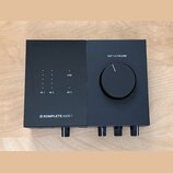 Černý audio rozhraní s matným povrchem. Na horní části jsou nápisy OUT 1/2 VOLUME, USB, 48 V a označení vstupů IN 1 a IN 2 u sloupců s kontrolkami. V…