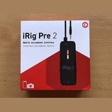 Fotografie znázorňuje krabici s produktem iRig Pre 2. Na bílo-červeném obalu je uveden název „iRig Pre 2“ a popis „Mobile microphone interface / Inte…