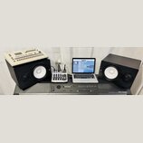 Sestava hudebního vybavení na šedém podkladu. V popředí je digitální piano s nápisem ROLAND DIGITAL PIANO RD-1000. Nad ním jsou dva černé studiové mo…