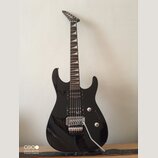 Černá elektrická kytara s dvojstupňovitým úhlem hlavy a hrotovými polohovými značkami na hmatníku. Na těle jsou dva humbuckery, ovládací knoflíky a t…