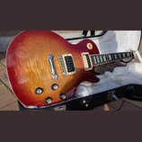 Elektrická kytara s tvarem single-cutaway a povrchovou úpravou v červeně-žlutém sunburstu s viditelnou strukturou dřeva. Nástroj má dva humbuckery v…