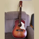 Akustická kytara s dreadnought tělesem v červeně-žlutém sunburst provedení a bílým pickguardem. Hmatník je tmavý s bílými tečkovanými značkami a hlav…